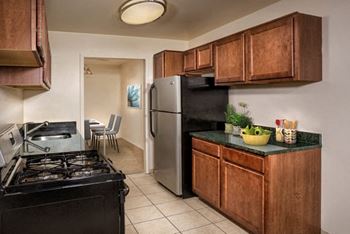 A kitchen with a black stove top oven, a refrigerator, and wooden cabinets.